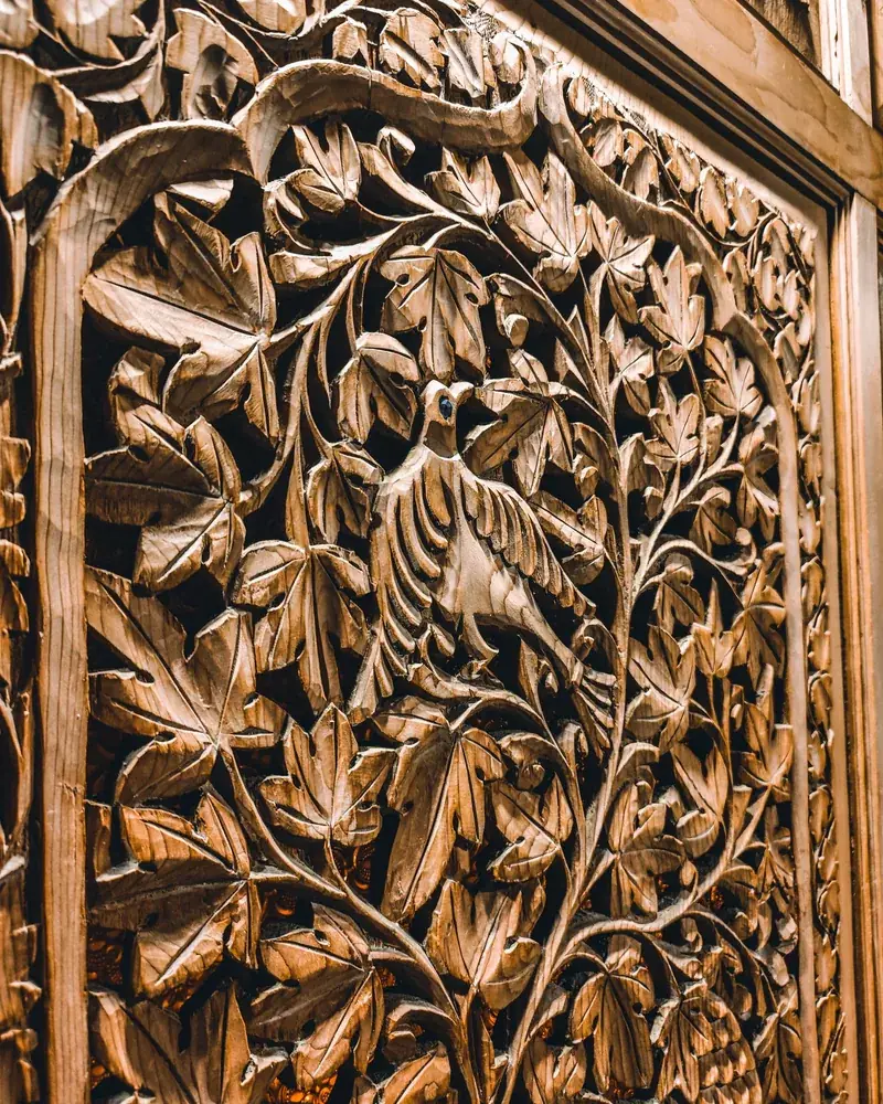 Detail vyřezávaného rostlinného ornamentu s ptačím motivem na dřevěném panelu